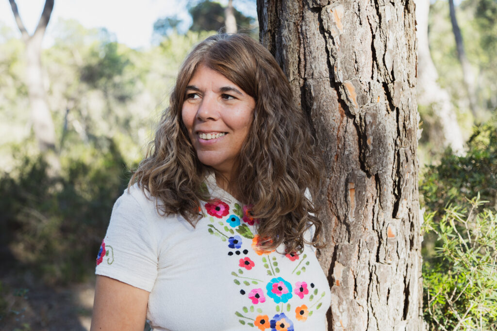 Adriana sonriendo apoyada en un tronco de un árbol